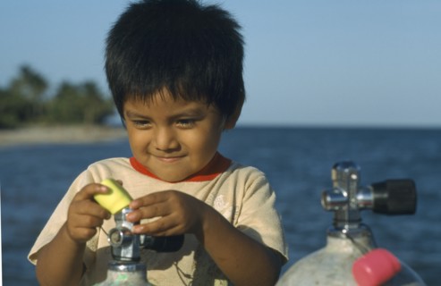 BELIZE, Placencia, Local boy playing with dive tanks