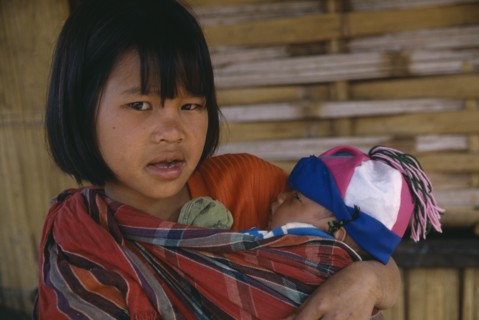 THAILAND, North, Chiang Rai , Lahu girl carrying baby in sling across her front.