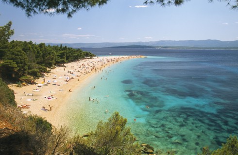 CROATIA, Brac Island, Bol, View over Zlatni Rat Beach lined with trees and scattered bathers