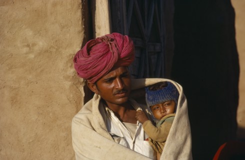 INDIA, Rajasthan, People, Man holding child wrapped in shawl on cold morning.