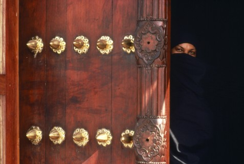 TANZANIA, Zanzibar Island, Zanzibar, Woman in full chandor looking out from behind ornate carved