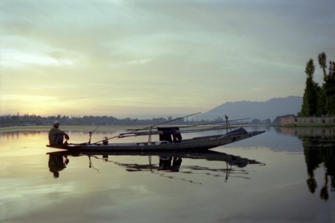 INDIA, Kashmir, Srinagar, Nagin Lake. Fisherman sitting at the very end of his canoe in the evening