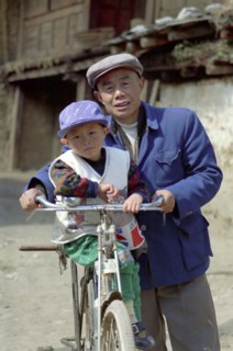 CHINA, Yunnan, Lijiang, Portrait of a man standing with a small boy on his bike holding a Pepsi