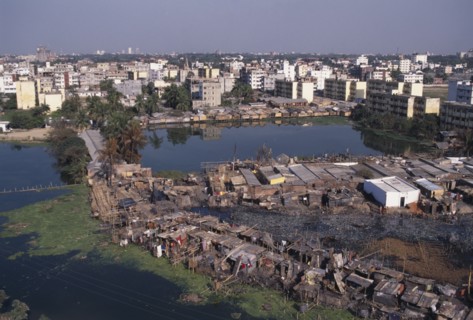 BANGLADESH, Dhaka, Waterside slum dwellings after fire with city buildings beyond.