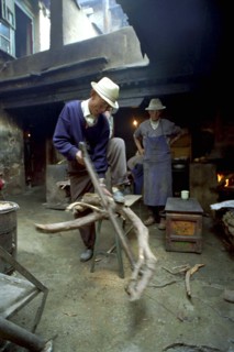 CHINA, Tibet, Lhasa, Elderly man cutting firewood for the kitchen in a courtyard