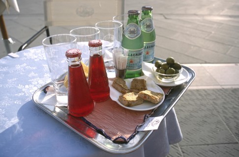 ITALY, Trieste, Piazza Unita, Tray on a small round lace clothed table with glasses and two bottles