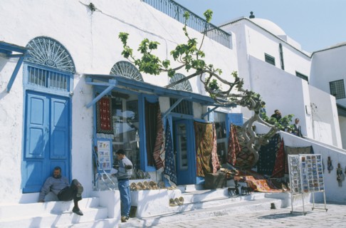 TUNISIA, Sidi Bou Said, Rugs and postcards for sale.  White painted shopfront with blue doors.  Two