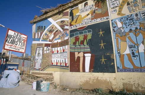 EGYPT, Dra Abul Naga, Painted mural on exterior wall of alabaster shop with man crouched down