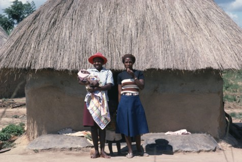 ZIMBABWE, General, Young Shona women and children standing outside thatched hut.