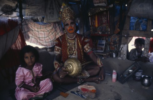 INDIA, Gujarat, Bhavnagar, Man in his shanty house dressed up as the Hindu deity Hanuman.  Child