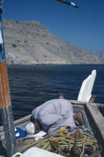 OMAN, Musandum, Fisherman praying on deck of boat.
