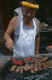 JAPAN, Honshu, Tokyo, Tsukiji Fish Market. Man cooking red meat on an open grill