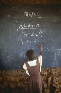 GHANA, West, Education, Child in primary school maths class writing sums on blackboard with chalk.