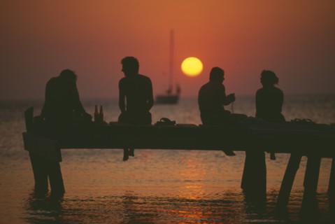 HONDURAS, Bay Islands, Roatan, Tourists sitting on jetty at West End silhouetted against warm