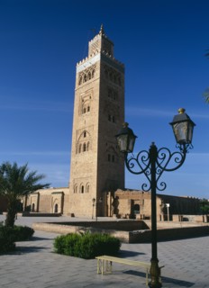 MOROCCO, Marrakech, Koutoubia Mosque tower seen from pavement with blue sky behind and street lamps