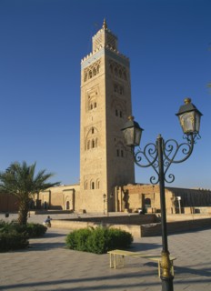 MOROCCO, Marrakech, Koutoubia Mosque tower seen from pavement with blue sky behind and street lamps
