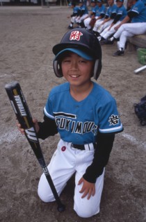 JAPAN, Honshu, Tono, Young boy kneeling on the grass wearing a Baseball kit holding a bat