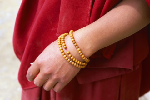 TIBET, Shigatse, Detail of a monks hand with a rosary wrapped around his wrist wearing a red robe.