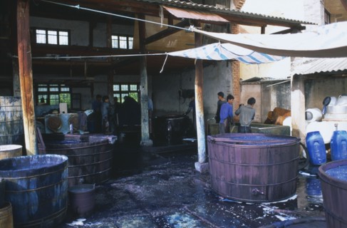 CHINA, Yunnan , Dali, Weishan. Batik factory with men working around  vats of dye under ornings.