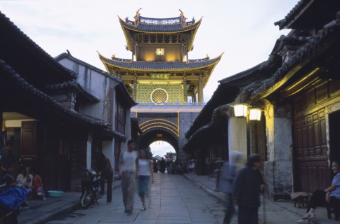 CHINA, Yunnan, Dali., Weishan. View down street at dusk towards an illuminated tower with people