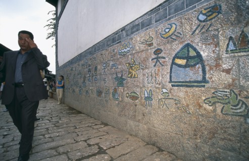 CHINA, Yunnan, Lijiang, Old town Naxi pictogram writing on a wall with a man dressed in a suit