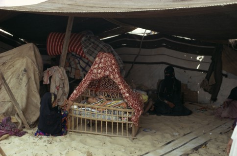 MIDDLE EAST, People, Bedouin desert encampment.  Woman and children inside tent with baby in
