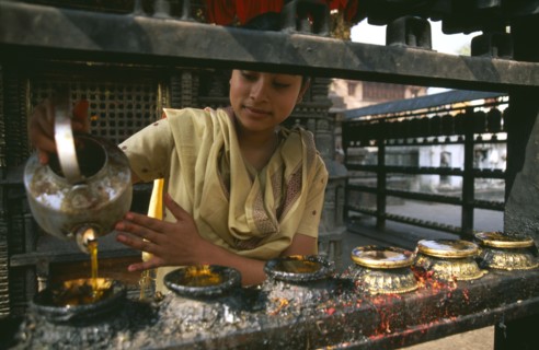 NEPAL, Swayambunath, "Young girl filling butterwick candles in shrine dedicated to Hariti, known