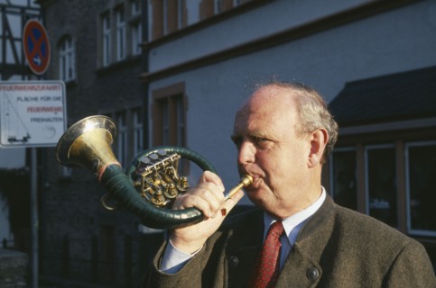 GERMANY, Rheinland Pfalz, Bernkastel, Man blowing hunting horn in town in the Mosel Valley.