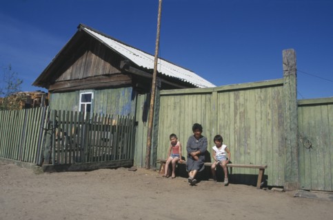 RUSSIA, Siberia, Lake Baikal, Buryat woman and children outside painted wooden fence of house.  The