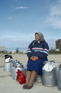 ESTONIA, Work, Woman sitting on milk cans waiting for ferry on the Baltic Coast.
