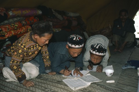AFGHANISTAN, Tribal People, Kirghiz children writing inside yurt with man sitting beside doorway