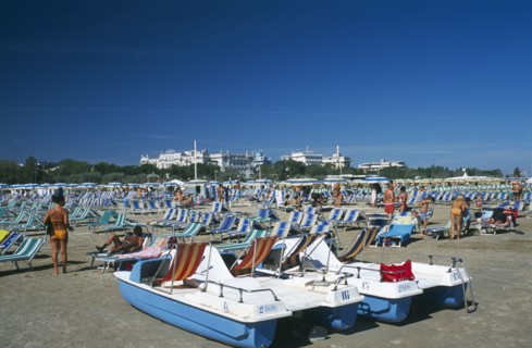 ITALY, Emilia-Romagna, Rimini, Busy beach scene with rows of striped sun loungers and pedalos in