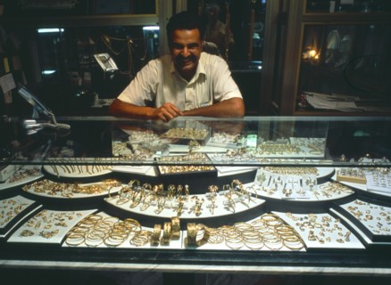 LIBYA, Zawia, Jeweller behind display of gold items in glass topped cabinet.