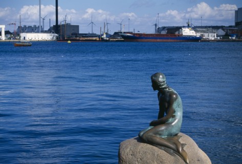 DENMARK, Zealand, Copenhagen, The Little Mermaid statue with port area and container ship behind.