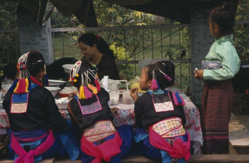 LAOS, Luang Prabang, Hmong girls in traditional dress eating at roadside foodstall.