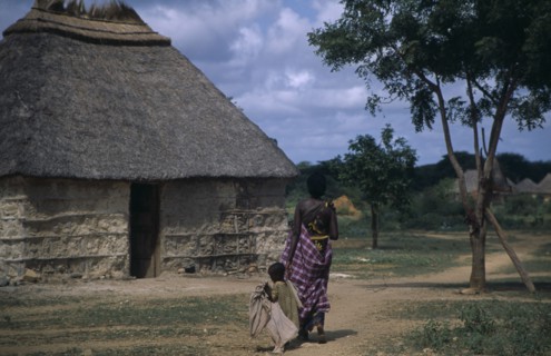 SOMALIA, Tribal People, Woman and child walking towards traditional thatchedhouse near Baidoa.