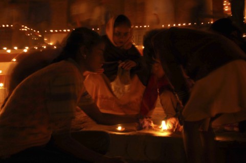 INDIA, Uttar Pradesh, Varanasi, Deep Diwali Festival with young girls lighting oil lamps on steps