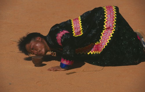 THAILAND, Chiang Mai, Hmong man blowing stones out of the way of his spinning top at Hmong New Year