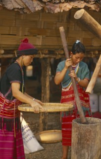 THAILAND, Chiang Mai, Sgaw Karen woman pounding rice by hand while another sifts with a large