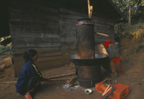 THAILAND, Chiang Rai Province, Doi Lan, Lisu woman stoking fire of her still for making corn