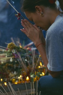THAILAND, Chiang Mai, Wat Jedi Luang, Inthakhin Ceremony. Worshiper praying beside offerings