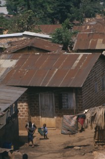 UGANDA, Kampala, Kamwoyke slum area.  Woman and child outside brick hut with corrugated iron roof.
