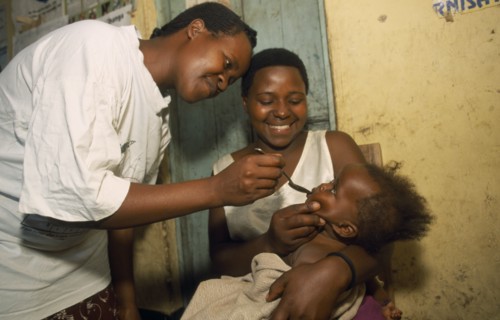UGANDA, General, Young child held by mother receiving medicine on spoon.