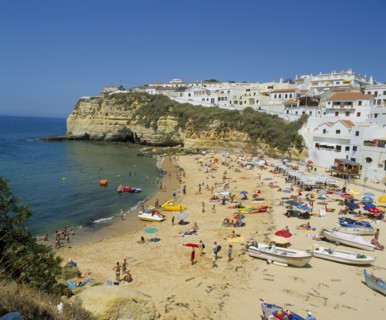 PORTUGAL, Algarve, Carvoeiro, White painted town on rocky headland overlooking busy beach.