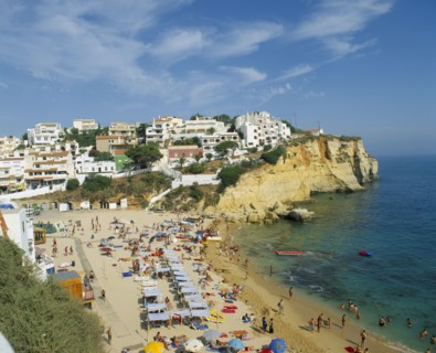 PORTUGAL, Algarve, Carvoeiro, White painted town on rocky headland overlooking busy beach.