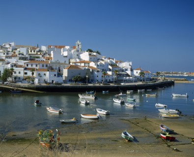 PORTUGAL, Algarve, Ferragudo, White painted town buildings overlooking harbour and moored boats.