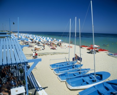 TUNISIA, Port el Kantaoui, Busy sandy beach with tourist boats and pedelos for hire and lines of