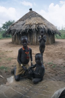 ETHIOPIA, Demeka, Hamer children sitting on animal skin outside thatched hut.
