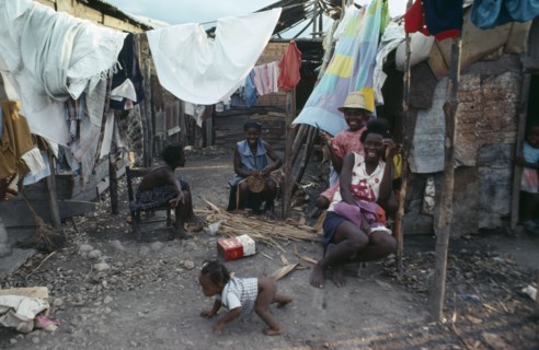 HAITI, People, Group of laughing women and children in shanty village sitting outside underneath