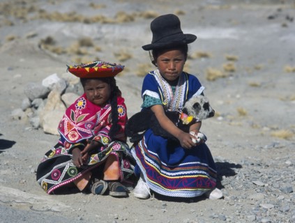 PERU, Near Arequipa, Two young children sitting on the ground with one holding a lamb